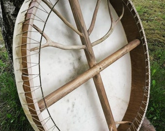 May include: A round, wooden frame drum with a white leather head. The drum has a wooden cross inside the frame and a tree branch design on the front.