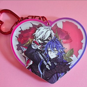 Puede incluir: Llavero en forma de corazón con un cierre rojo en forma de corazón. El llavero presenta una ilustración de estilo anime de dos personajes, uno con cabello blanco y el otro con cabello azul, sobre un fondo de rosas rojas secas. El borde es rosa y morado.