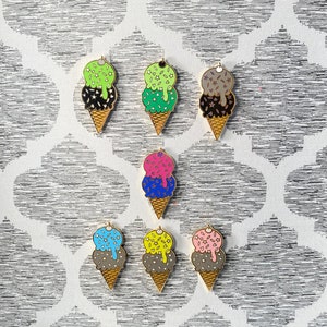 May include: Set of ten enamel pins featuring ice cream cones with different colored scoops and sprinkles. The pins are gold-toned and have a shiny finish.