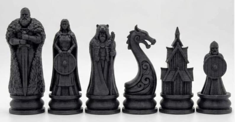 May include: A black Viking-themed chess set. The pieces depict a king, queen, bear, dragon, church, and warrior. Each piece is on a round base. The set is made of a dark material, with each piece measuring approximately 7-10 cm in height.