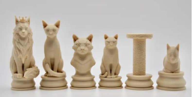 以下が含まれることがあります： ベージュ色の猫をテーマにしたチェスの駒のセット。王冠をかぶったライオン、座っている猫、猫の胸像、別の座っている猫、爪とぎ、小さな猫のフィギュアが含まれています。白い背景です。
