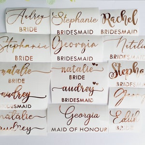 K&ouml;nnte beinhalten: Ein Satz mit 12 Aufklebern aus ros&eacute;goldener Folie mit Namen und Titeln f&uuml;r eine Hochzeitsgesellschaft. Die Namen sind Audrey, Stephanie, Rachel, Georgia, Natalie und Edith. Die Titel sind Braut, Brautjungfer und Maid of Honor.