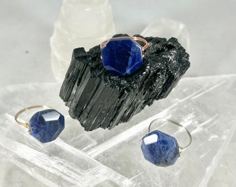 May include: Three rings with blue gemstone settings. The rings are made of gold and silver wire and feature different sized hexagonal shaped stones. The rings are displayed on a white crystal surface.