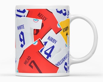 May include: White ceramic mug with a colorful design of soccer jerseys featuring player names and numbers, including "Kelly", "White", "Earp", "Kirby", "Mead", and "Williams".