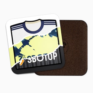 Puede incluir: Una camiseta de fútbol blanca y negra con cuello azul y un diseño abstracto amarillo y azul. La camiseta está rasgada en el medio, revelando el diseño a rayas blanco y negro debajo. El texto "SBTOP" está impreso en la camiseta.