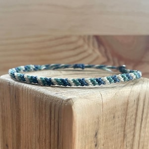 Può includere: Un braccialetto dell'amicizia intrecciato con fili bianchi, blu e verdi.