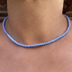 Puede incluir: Un collar de cuentas azul claro hecho de pequeñas cuentas redondas. El collar lo lleva una persona, pero no se ve el rostro de la persona.