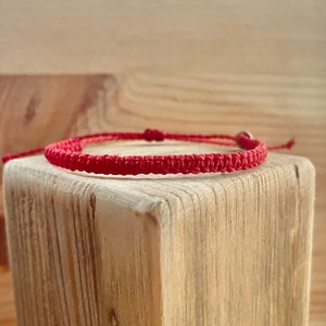 Könnte beinhalten: Ein rotes geflochtenes Armband mit einem silbernen Verschluss. Das Armband liegt auf einer Holzoberfläche.