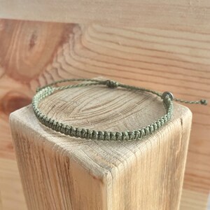 Könnte beinhalten: Ein geflochtenes Armband aus grünem Kordel mit einem silbernen Verschluss.