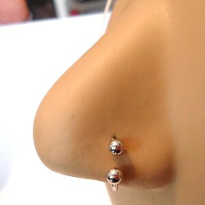 May include: A silver nose ring with two round balls. The ring is curved and goes through the nostril.
