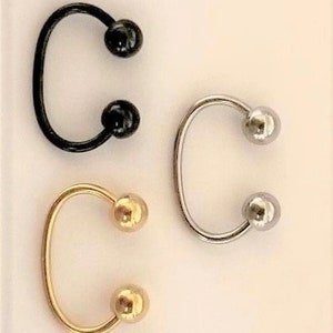 May include: Three horseshoe shaped earrings with ball ends. The earrings are black, silver, and gold.
