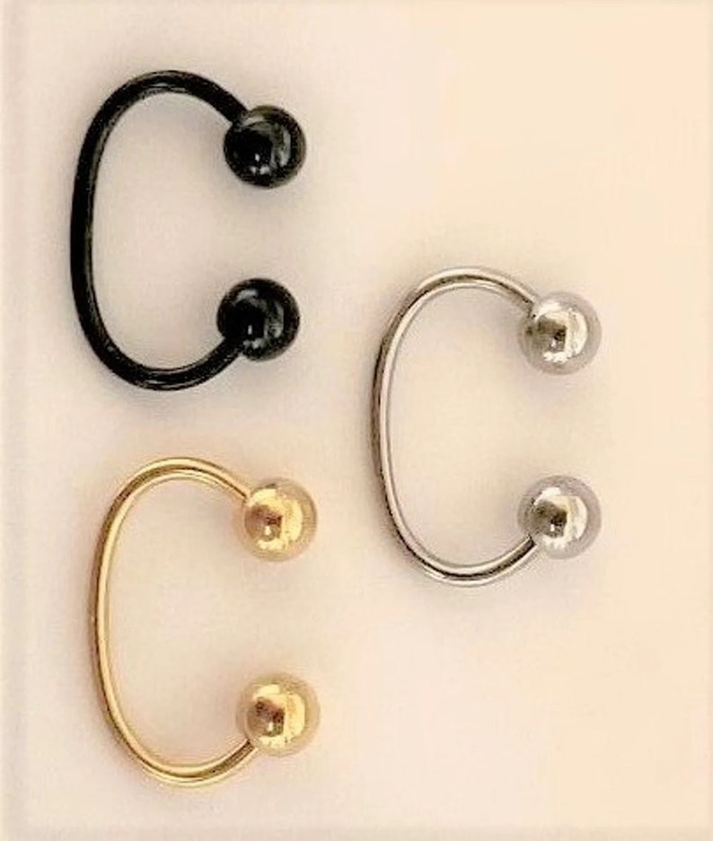 May include: Three horseshoe shaped earrings with ball ends. The earrings are black, silver, and gold.