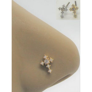 May include: A gold nose ring with a clear crystal cross design. The cross is made up of small, clear crystals set in a gold metal setting.