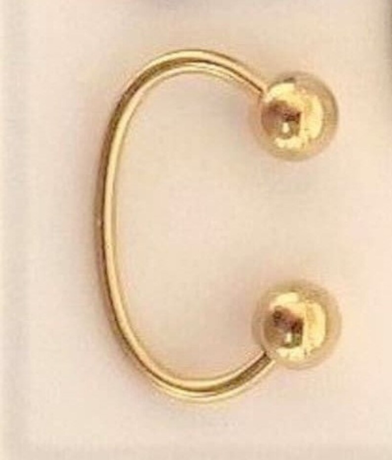 May include: Gold-toned hoop earring with two round balls at the ends.