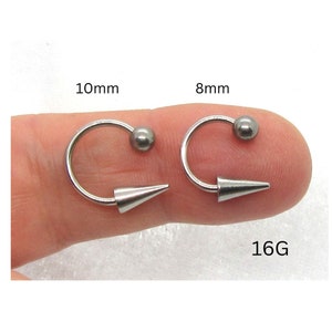 Puede incluir: Dos piezas de joyer&iacute;a corporal plateadas con una punta puntiaguda y una bola en el otro extremo. Las piezas tienen un di&aacute;metro de 8 mm y 10 mm y son de calibre 16.