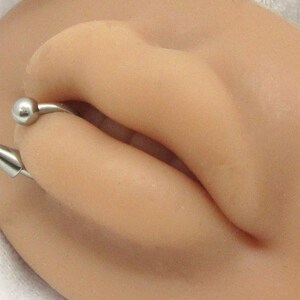 Puede incluir: Un anillo de labio plateado con una peque&ntilde;a bola en un extremo y una punta puntiaguda en el otro extremo.