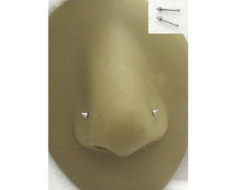 May include: A close-up of a nose piercing on a mannequin head. The piercing is a silver stud with a pointed tip. The mannequin head is a light brown color.