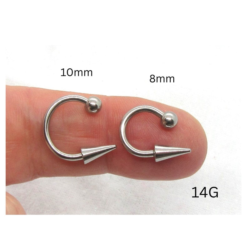 Puede incluir: Dos anillos de nariz de acero quir&uacute;rgico plateado de 14G con un extremo c&oacute;nico y una bola en el otro extremo. Los anillos tienen un di&aacute;metro de 8 mm y 10 mm.