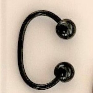 May include: A black horseshoe-shaped ring with two black ball ends.