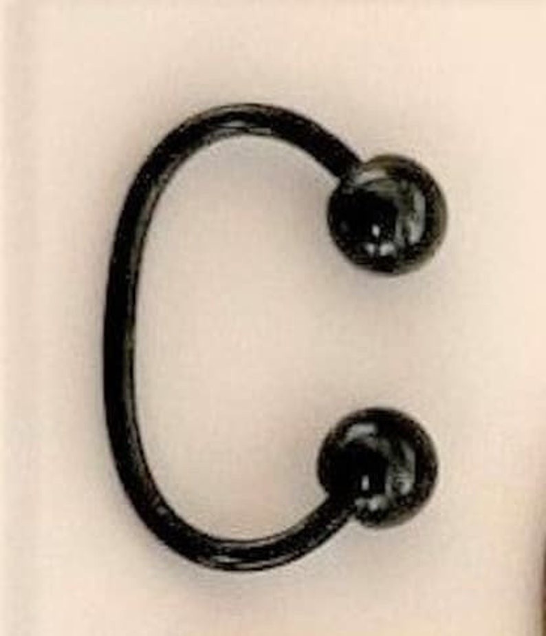 May include: A black horseshoe-shaped ring with two black ball ends.