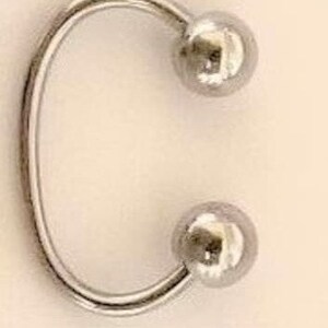 May include: A silver metal ring with two round balls on either end.