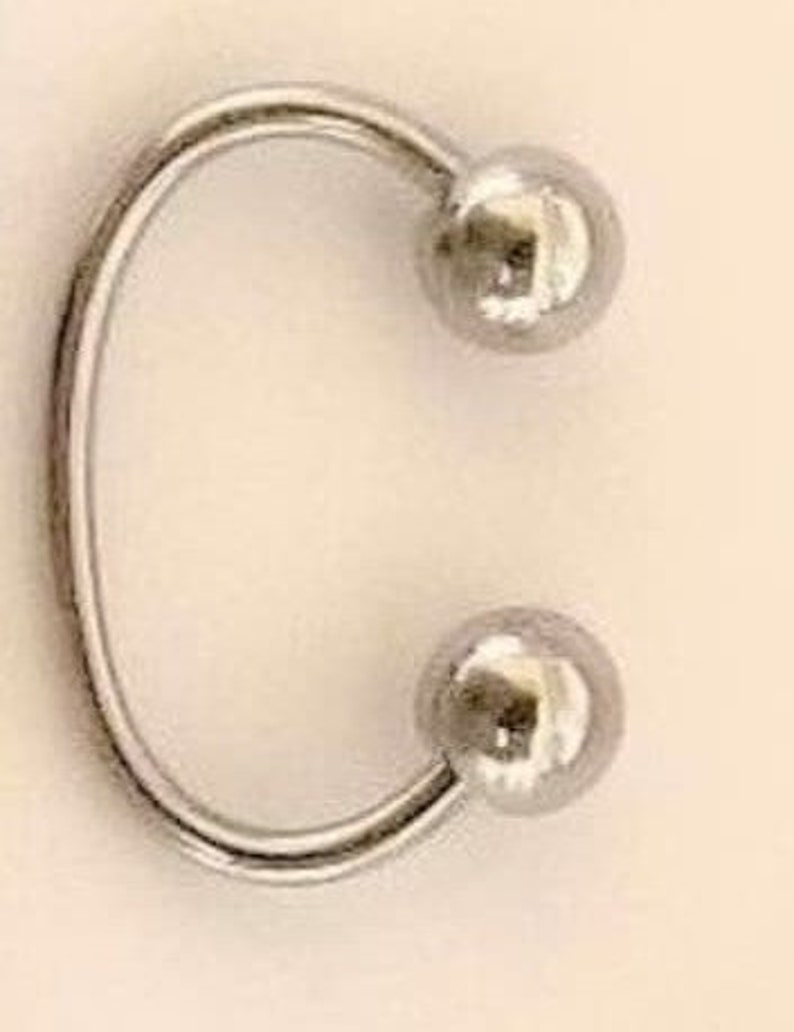 May include: A silver metal ring with two round balls on either end.