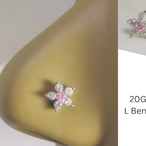 May include: A close-up of a nose piercing with a pink and clear flower design. The piercing is a 20 gauge L bend.
