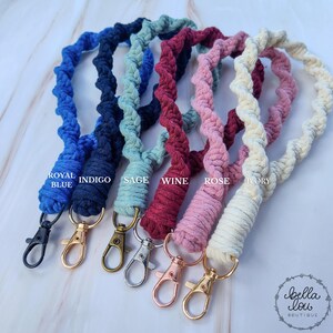May include: Seven colorful crocheted keychains with metal clasps. The colors are royal blue, indigo, sage green, wine red, rose pink, ivory, and white. The keychains are arranged in a row from left to right.