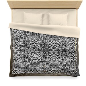 May include: Overhead view of a bed with a light wood headboard, cream-colored bedding, and two pillows. The bedspread features a black and white leopard print design with a gold border. The bed is set against a white background.