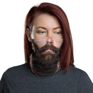 May include: A woman with long red hair is wearing a black neck gaiter with a printed image of a man's face with a beard and mustache.