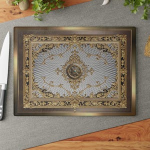 May include: Rectangular cutting board with an ornate, gold-colored design on a light blue background. The design features intricate floral patterns and a central medallion. The border is a dark brown with a gold trim.