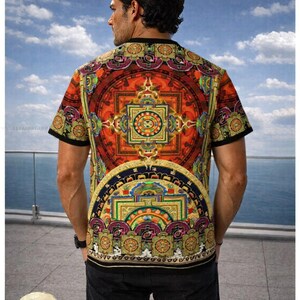 May include: A short-sleeved t-shirt featuring a vibrant, intricate mandala-inspired print in shades of orange, red, gold, and purple. The design includes geometric patterns and circular motifs across the back and sleeves, finished with a black trim.