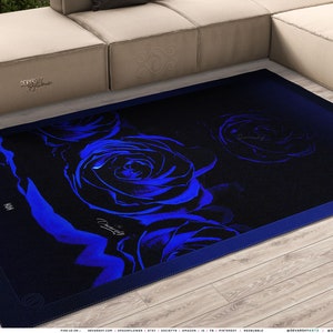 May include: A rectangular area rug featuring a dark black background with vibrant blue rose floral patterns. The design includes a prominent blue rose in the center and a smaller one to the right, with a blue border and a signature logo on the surface.