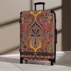 May include: A rolling suitcase featuring a vibrant, multi-colored paisley pattern in shades of yellow, red, green, and blue. The luggage has a black frame, a retractable handle, and four wheels. The text "DEVARSHY" is printed on a horizontal band.