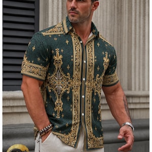 May include: Green button-down shirt with a gold baroque pattern. The short-sleeved shirt has a classic collar and is paired with light-colored pants. The shirt's design features ornate floral and scrollwork elements.