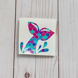 May include: A teal, pink, and purple mermaid tail sticker with a scale pattern. The tail is in a water splash design.
