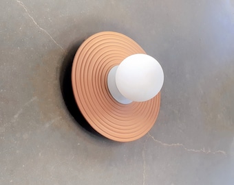 May include: A round, white frosted glass light fixture with a terracotta-coloured, circular base with concentric rings.