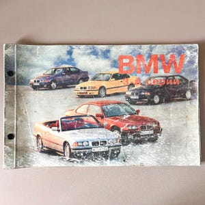 Könnte beinhalten: Eine alte BMW 3er Serie Broschüre mit verschiedenen Automodellen in verschiedenen Farben, darunter Lila, Gelb, Rot und Schwarz. Das BMW-Logo ist oben prominent zu sehen, mit kyrillischem Text. Die Broschüre hat ein abgenutztes Aussehen.