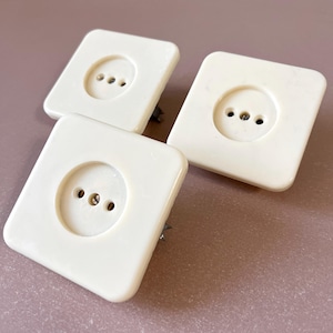 Può includere: Tre coperture per prese di corrente quadrate bianche con tre fori rotondi ciascuna.