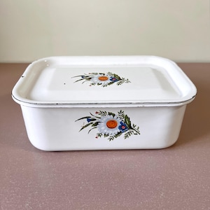 Puede incluir: Plato rectangular de esmalte blanco con tapa. El plato tiene un diseño floral con margaritas blancas y detalles azules y naranjas.