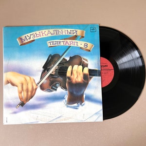 May include: A vinyl record album cover with a blue and white background featuring a hand holding a violin. The album title is "Музыкальный Телетайп - 8".