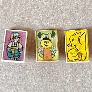 May include: Three small, rectangular vintage pins with cartoon images. One pin features a figure in a traditional outfit, another a smiling bee lifting weights, and the last a squirrel with a pumpkin.