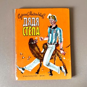 May include: A vintage book cover with an orange background. The cover features an illustration of a man in a striped shirt and white pants riding a camel. The title "ДЯДЯ СТЁПА" is prominently displayed in large, yellow letters.