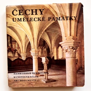以下が含まれることがあります： 「ČECHY UMĚLECKÉ PAMÁTKY」というタイトルが大きく太字で書かれたヴィンテージ本の表紙。アーチ型の天井と柱がある大聖堂の内部の写真が使われています。追加のテキストには「ПАМЯТНИКИ ИСКУССТВА」、「KUNSTDENKMÄLER」、および「ART MONUMENTS」が含まれています。
