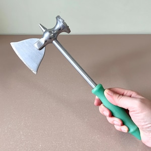 Puede incluir: Un ablandador de carne plateado con un mango verde. El ablandador tiene una cabeza plana y ancha con un borde dentado y un extremo puntiagudo.