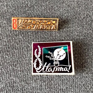 Könnte beinhalten: Zwei Vintage-Anstecknadeln. Die erste ist rechteckig, goldfarben, mit der Zahl "8" in Rot und dem kyrillischen Wort "MAPTA". Die zweite Anstecknadel ist quadratisch, mit einer weißen "8" und dem kyrillischen Wort "Mapma!" und einem floralen Design.