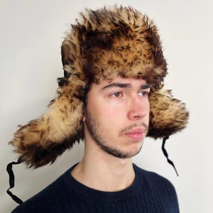 May include: A brown and tan faux fur Ushanka hat with ear flaps and black ties. The hat is made of a soft, fluffy material and is designed to keep the head and ears warm. This winter hat is perfect for cold weather.