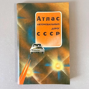 Puede incluir: Una cubierta de libro vintage de color naranja, azul y marrón con el título "Atlas avtomobil'nykh dorog SSSR" en letras doradas. Una ilustración en blanco y negro de un coche se encuentra en el centro de la cubierta.