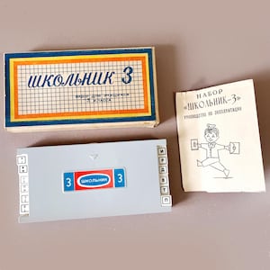 May include: A vintage educational set, featuring a box with the text "ШКОЛЬНИК 3" in blue and a grid pattern. A gray plastic case with the same text and a booklet with a cartoon illustration are also present.