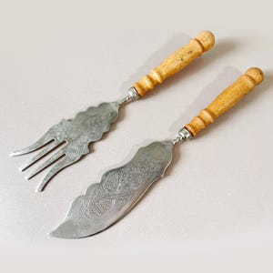 Peut inclure: Un ensemble de service vintage comprenant une fourchette et un couteau. Les ustensiles ont des lames argentées ornées de motifs décoratifs. Les manches sont en bois clair. L'ensemble est conçu pour servir.
